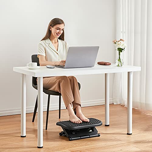 Woman sitting at a desk using a laptop with a footrest.